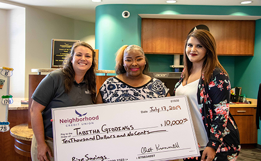 Three people standing around a big check smiling